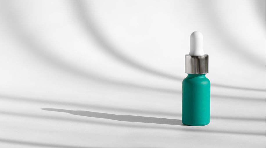 A teal bottle of anti-aging serum against a white background with shadows.