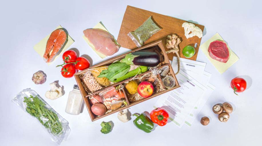 An overhead view of an opened food subscription box with food and recipe sheets.