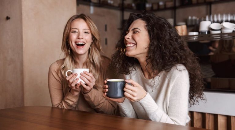 Two women holding coffee mugs and smiling while talking.