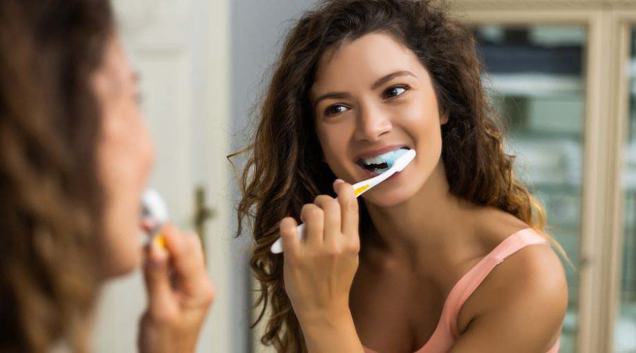 A girl brushing her teeth in front of a mirror.