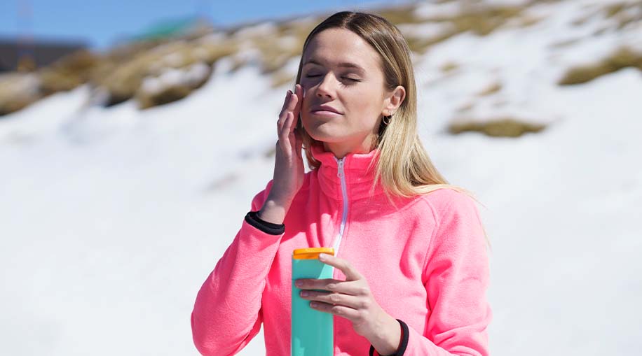 A woman wearing a UPF sweater and applying sunscreen to her face.